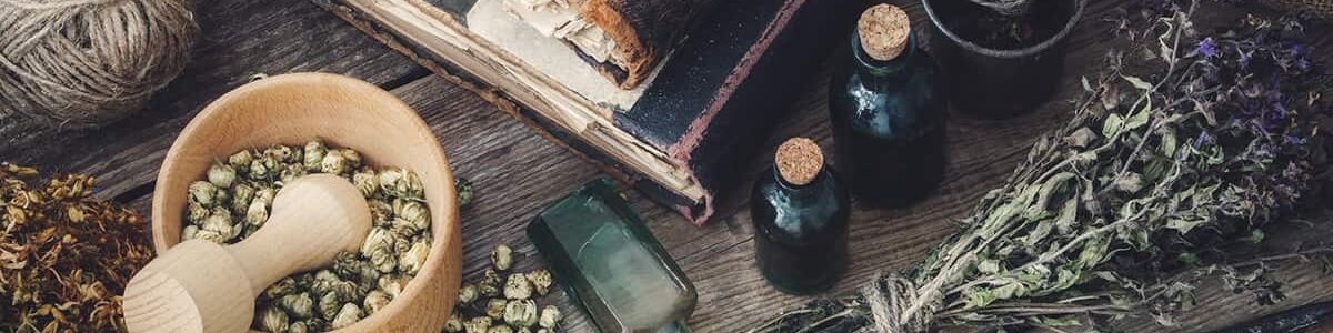 Tincture bottles, assortment of dry healthy herbs, old books, mortar, scissors on old wooden desk. Herbal medicine. Top view.